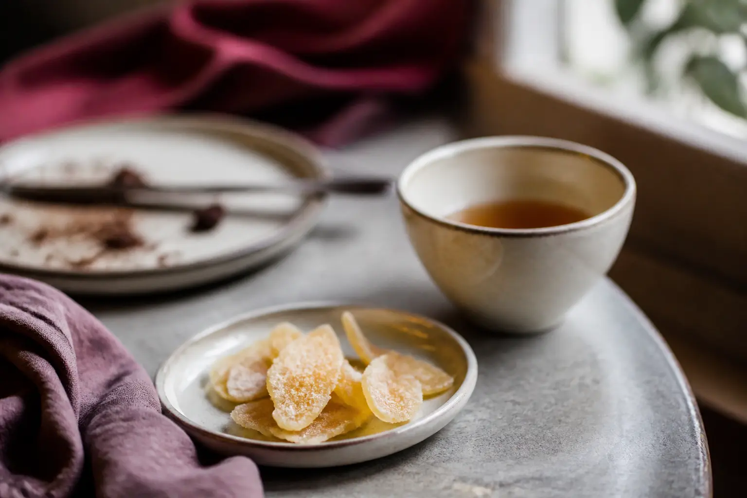Bienfaits du gingembre confit : tranches sur assiette près d’une tasse de thé, après un repas copieux, lumière douce.