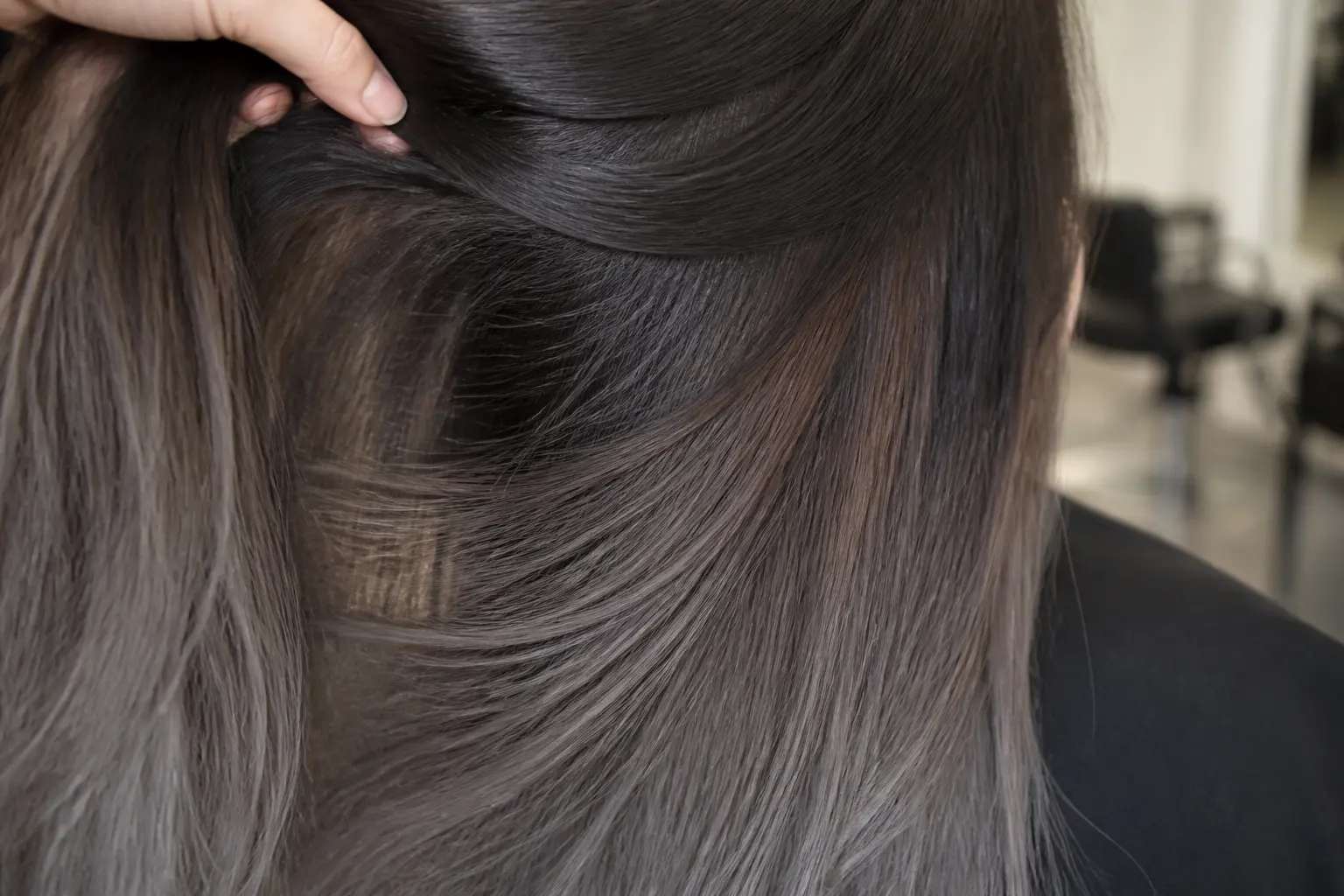 Cendré balayage gris sur brune : mèche brune en salon, dégradé gris cendré des racines aux pointes, lumière douce.