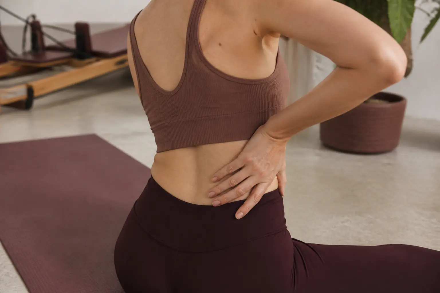 Pilates effets négatifs : personne sur un tapis, main au bas du dos après séance, gêne légère en salon lumineux