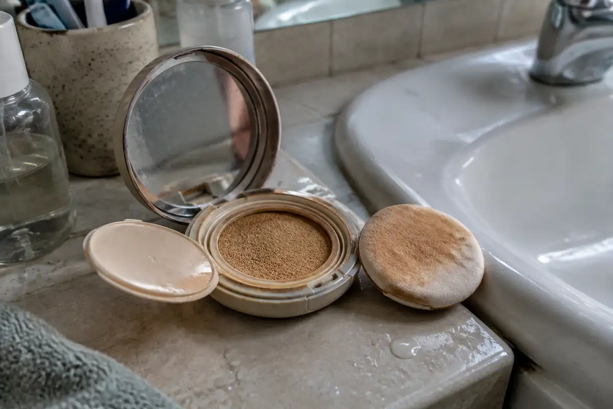 Boîtier de cushion ouvert au bord d'un lavabo, houppette tachée de fond de teint