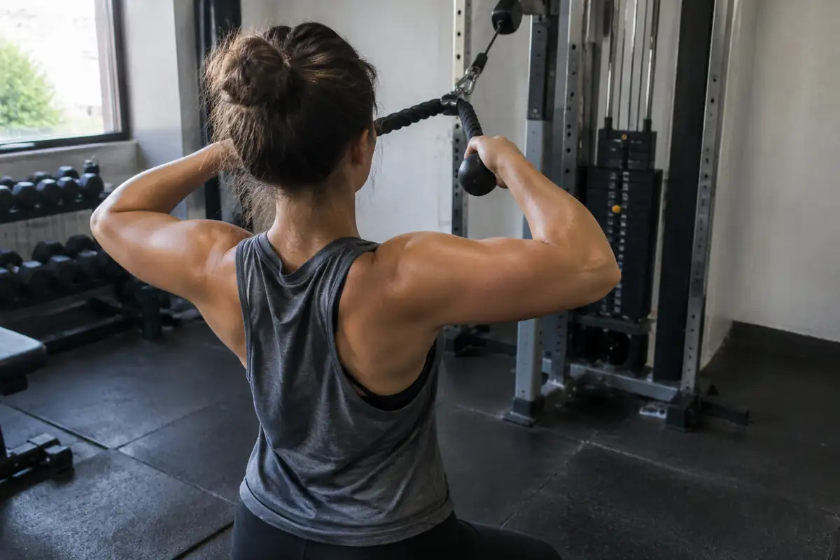 Personne vue de dos tirant une corde de poulie vers son visage dans une petite salle de sport